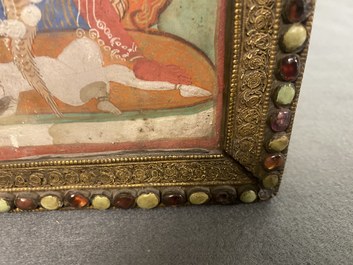 A Tibetan thangka in inlaid gilt brass frame, 19th C.